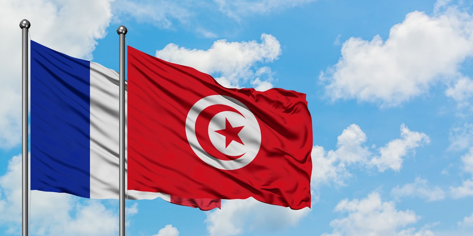 France and Tunisia flag waving in the wind against white cloudy blue sky together
